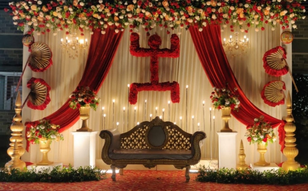 Elegant wedding stage setup with red and gold decor, chandeliers and floral arrangements